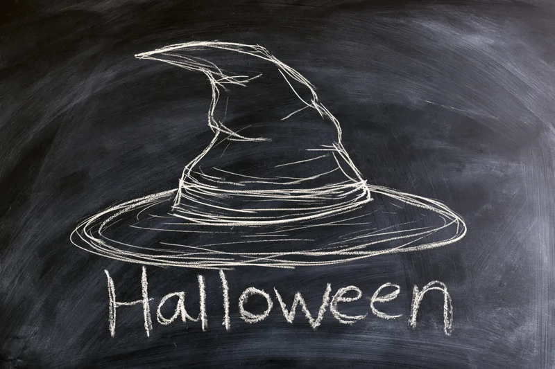 Chalk drawing of a witch hat with the word halloween written on a blackboard