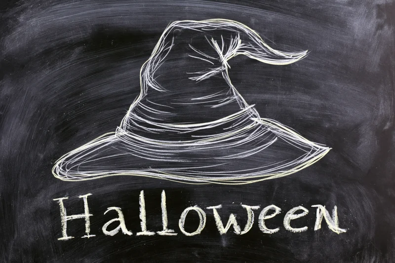 Chalk drawing of a witch hat with the word halloween written below on a blackboard