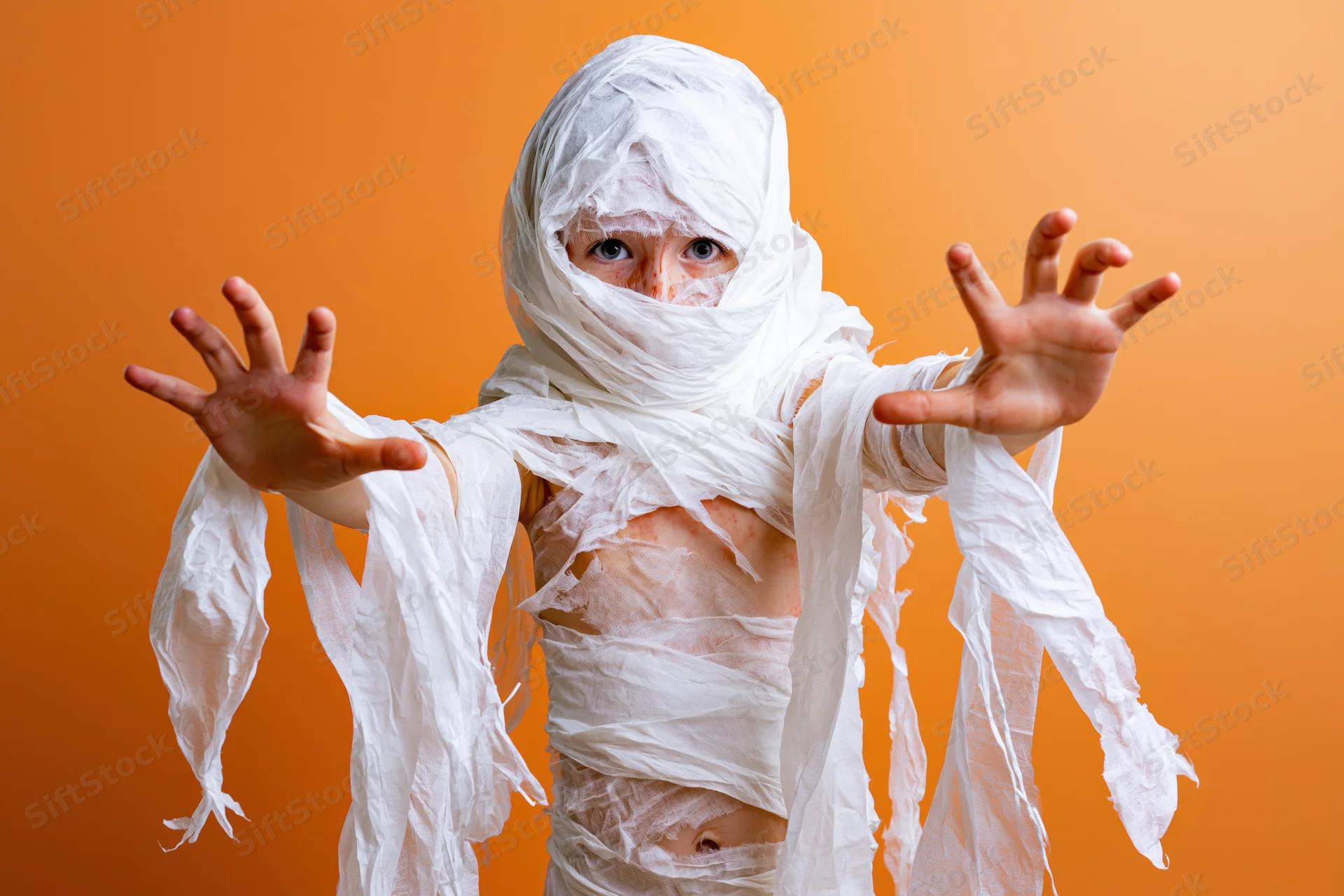 Child in homemade mummy costume with arms outstretched against orange background