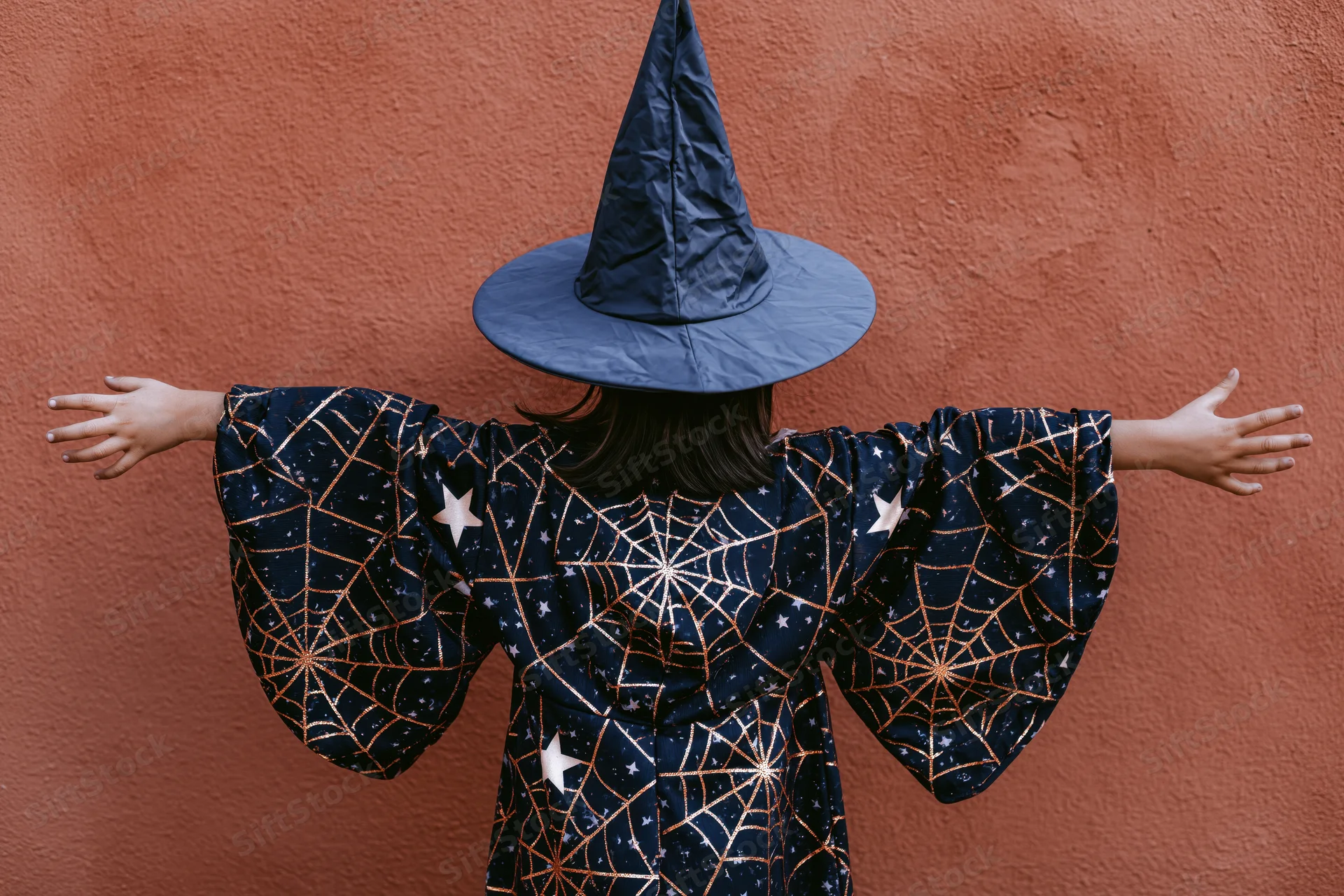 Child in witch costume with arms outstretched against textured wall