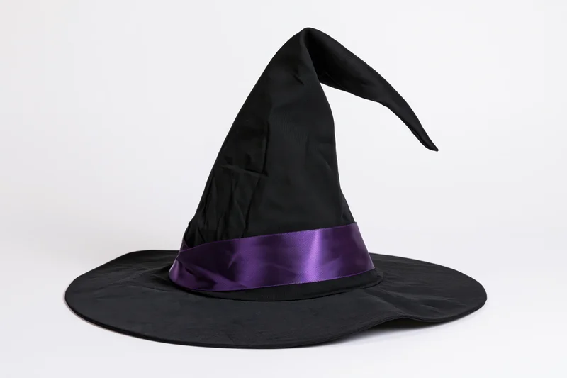 Black witch hat with curved pointed tip and purple satin band on white background