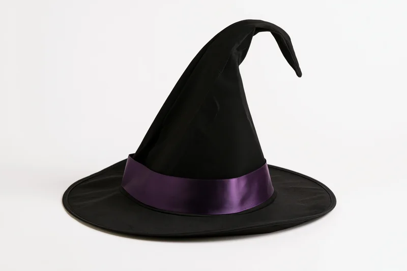 Black witch hat with curved tip and purple satin band on white background