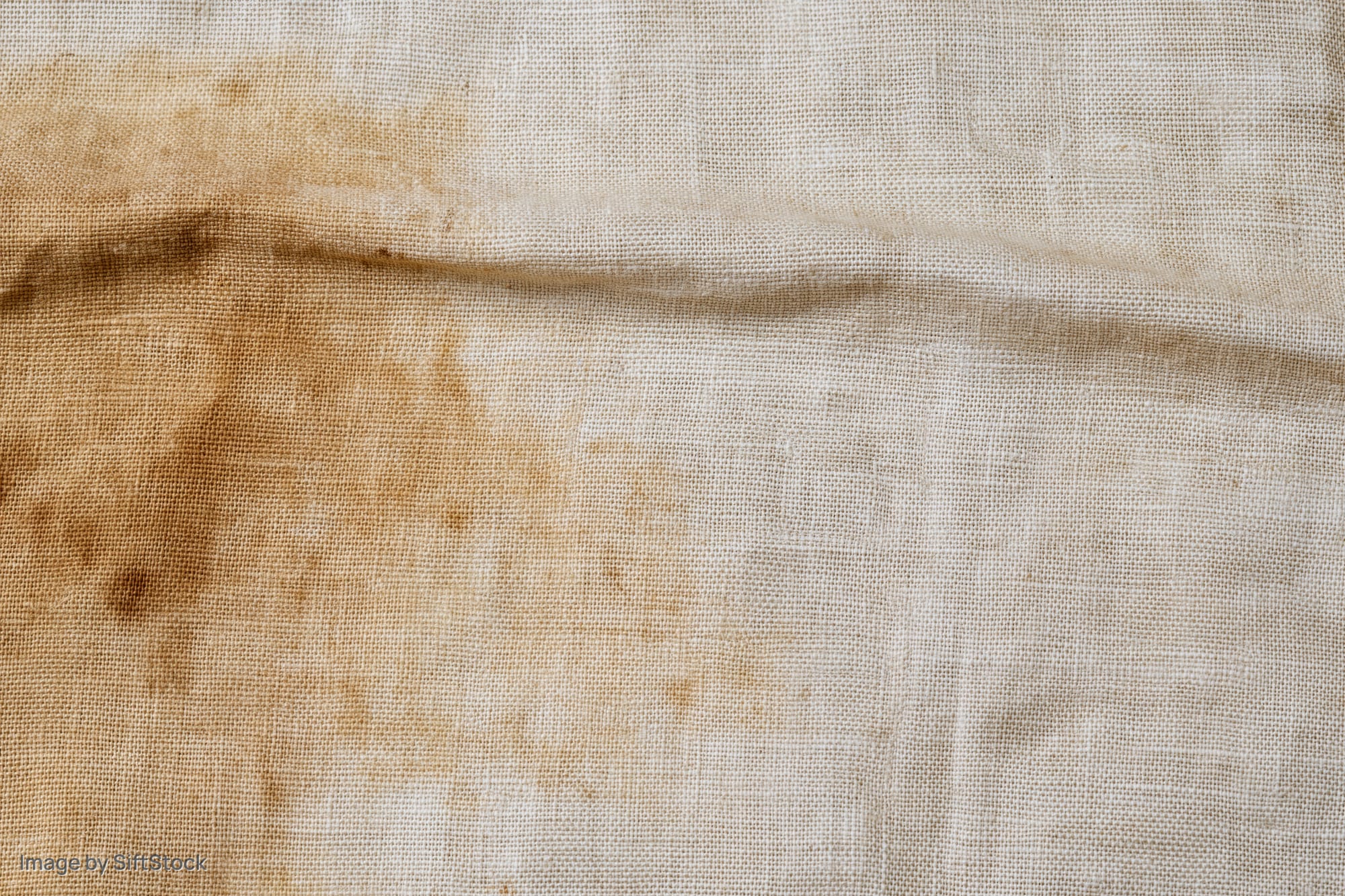 Close-up of aged linen fabric with brown stains and creases filling the frame