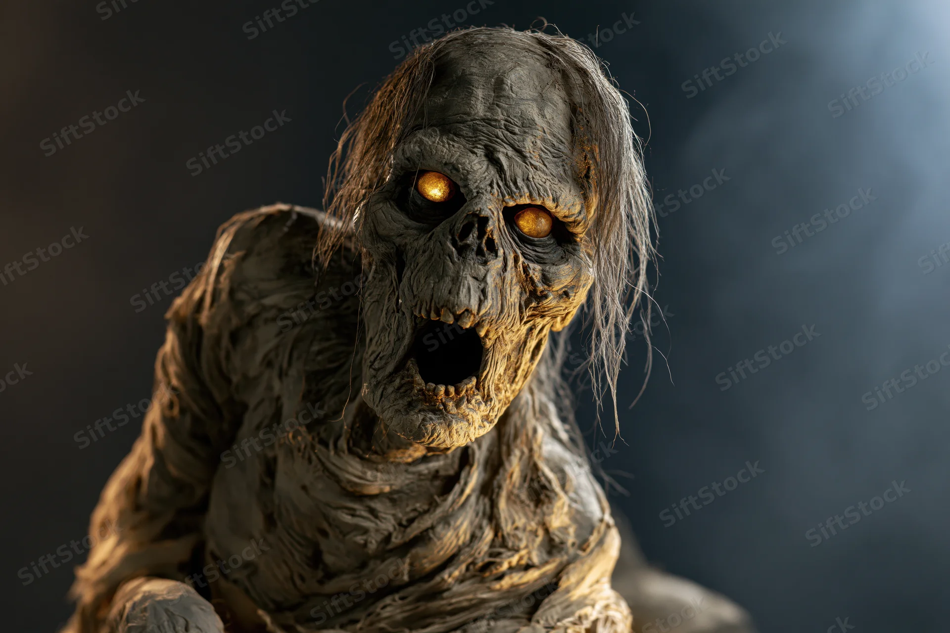 Decayed mummy creature prop with glowing eyes and open mouth against dark smoky background