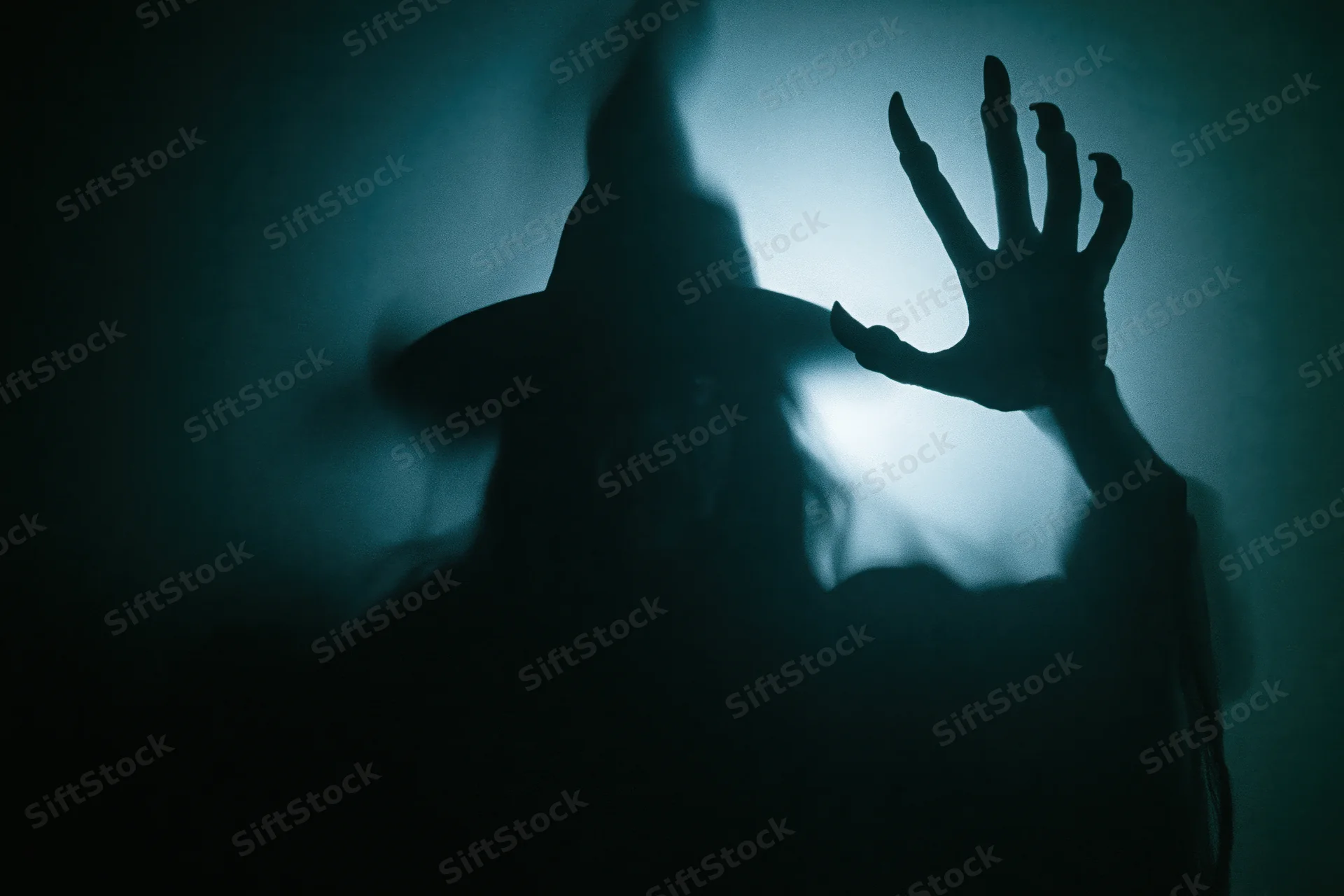 Dark silhouette of a witch with pointed hat and clawed hand pressed against a smoky surface