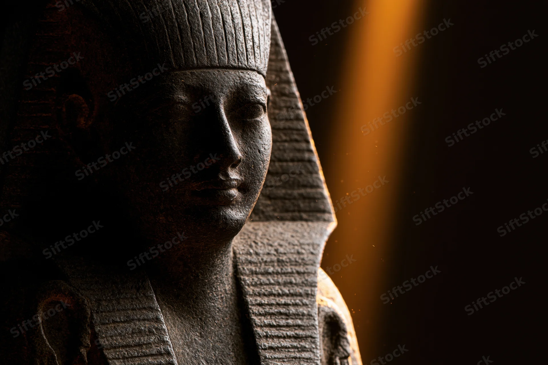Closeup profile of an ancient egyptian stone pharaoh statue in dramatic lighting