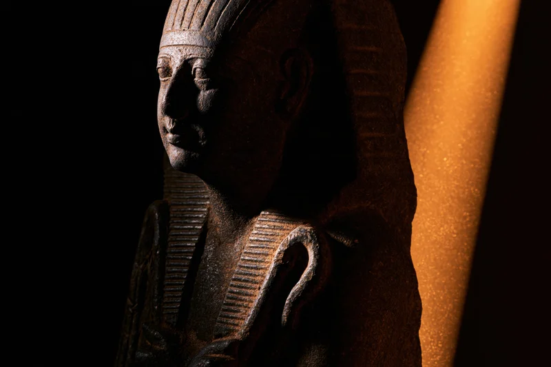 Dark stone egyptian pharaoh statuette with crook and flail in shadowed display