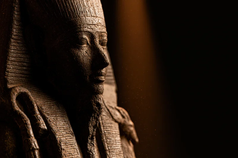 Closeup of dark stone egyptian pharaoh statue holding crook and flail in dim light