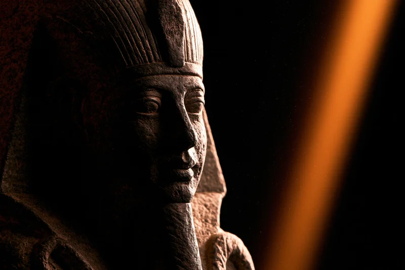 Close-up of an ancient egyptian pharaoh stone statue with nemes headdress in dim lighting
