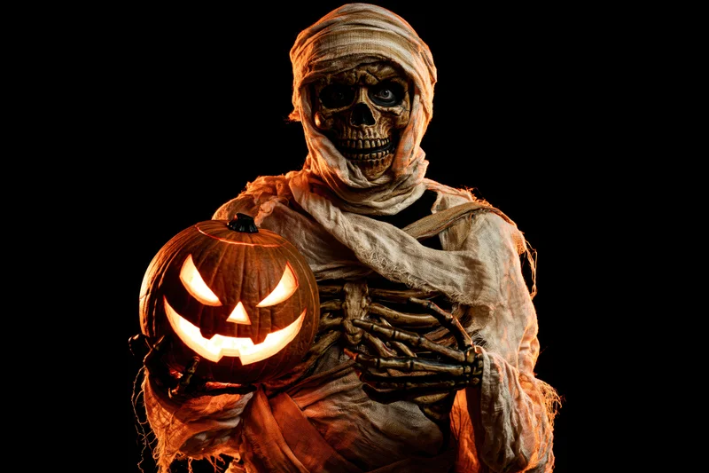Mummy in decayed bandages holding glowing jack-o-lantern against black background