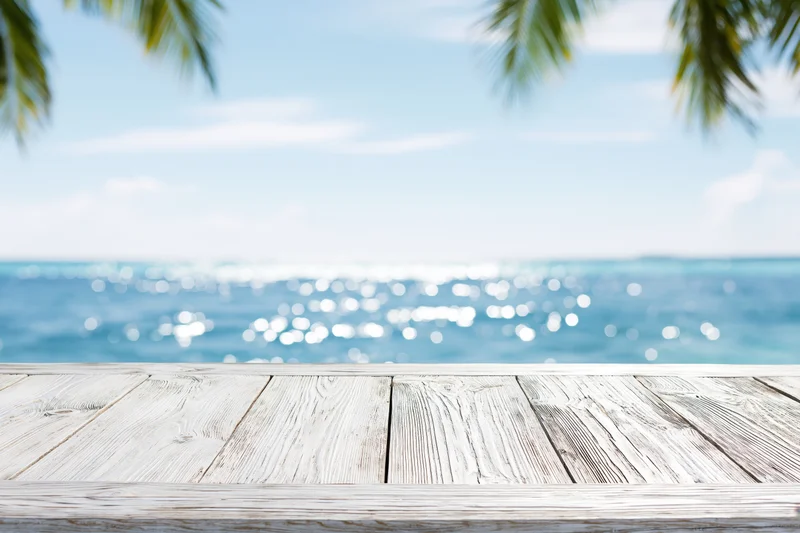 Weathered white wooden table surface overlooking ocean with palm fronds above