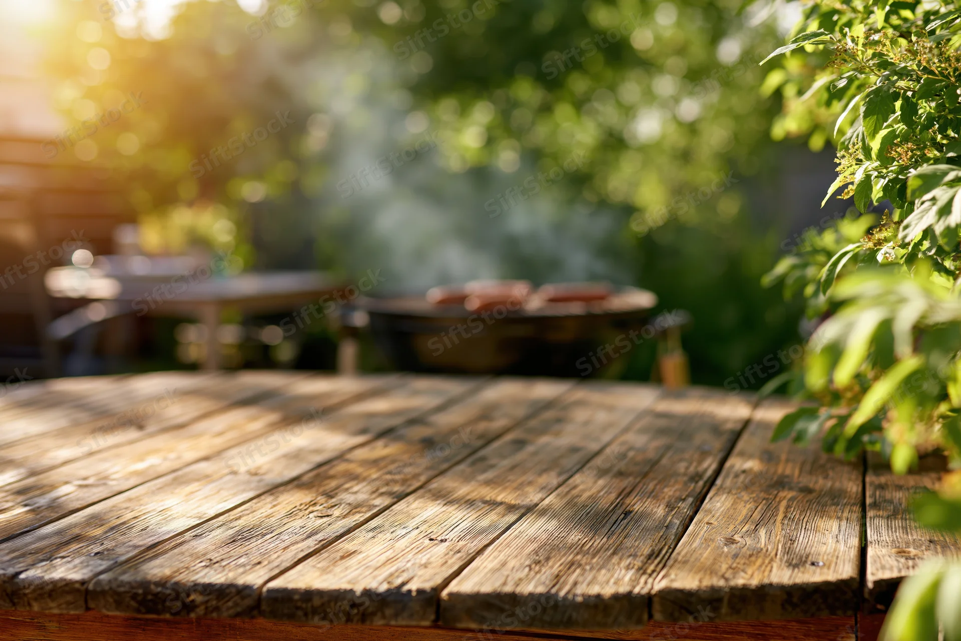 Weathered wooden table in a sunlit backyard with barbecue grill and greenery in the background