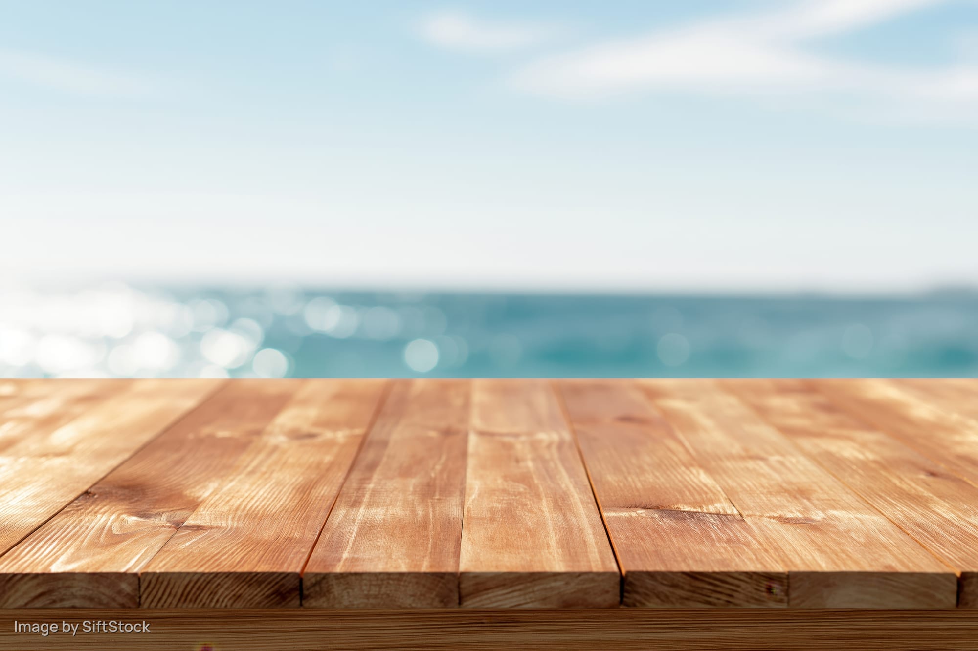 Wooden table surface in foreground with blurred ocean and sky background