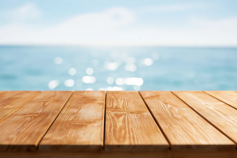 Wooden table surface in foreground with blurred ocean and sky background