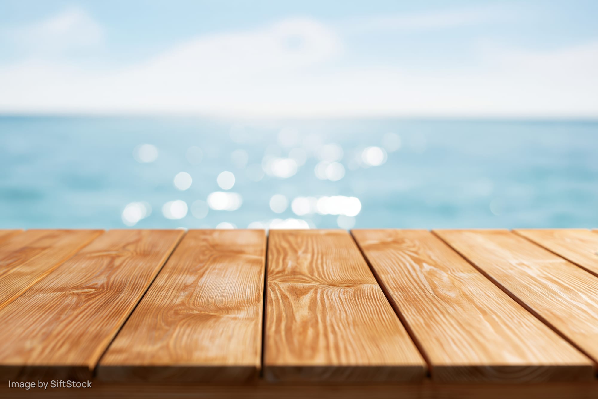 Wooden table surface in foreground with blurred ocean and sky background