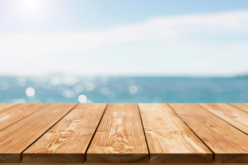 Wooden table surface in foreground with blurred ocean and sky background