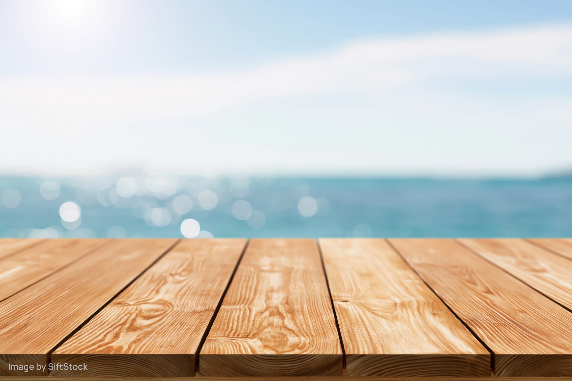 Wooden table surface in foreground with blurred ocean and sky background