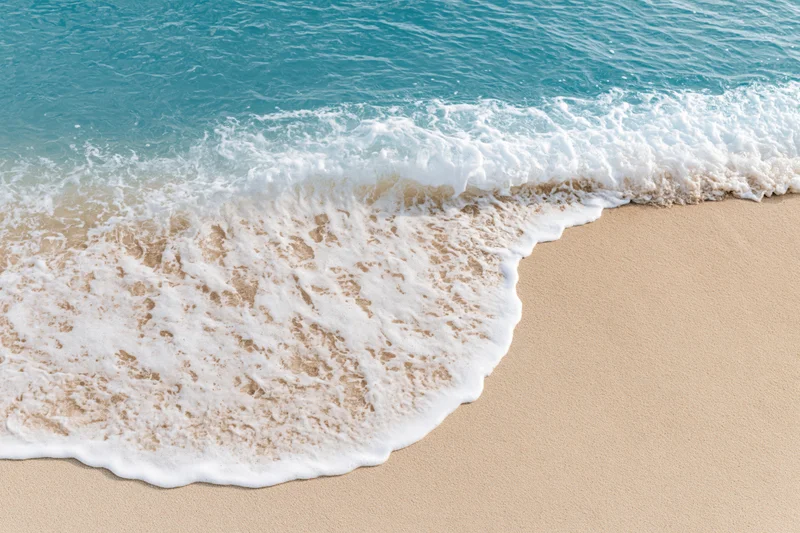 Gentle ocean wave washing onto clean sandy beach
