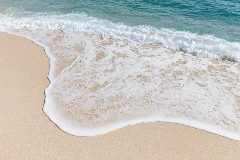 Gentle ocean wave washing onto clean sandy beach