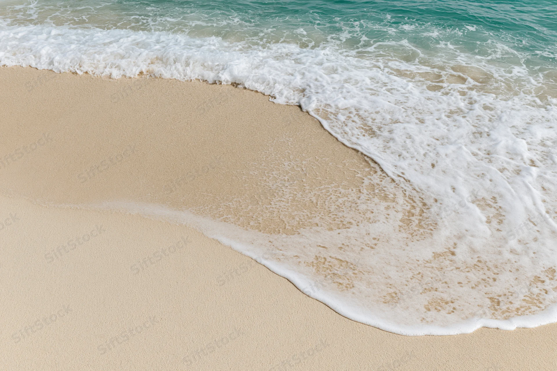 Gentle ocean wave washing onto clean sandy beach