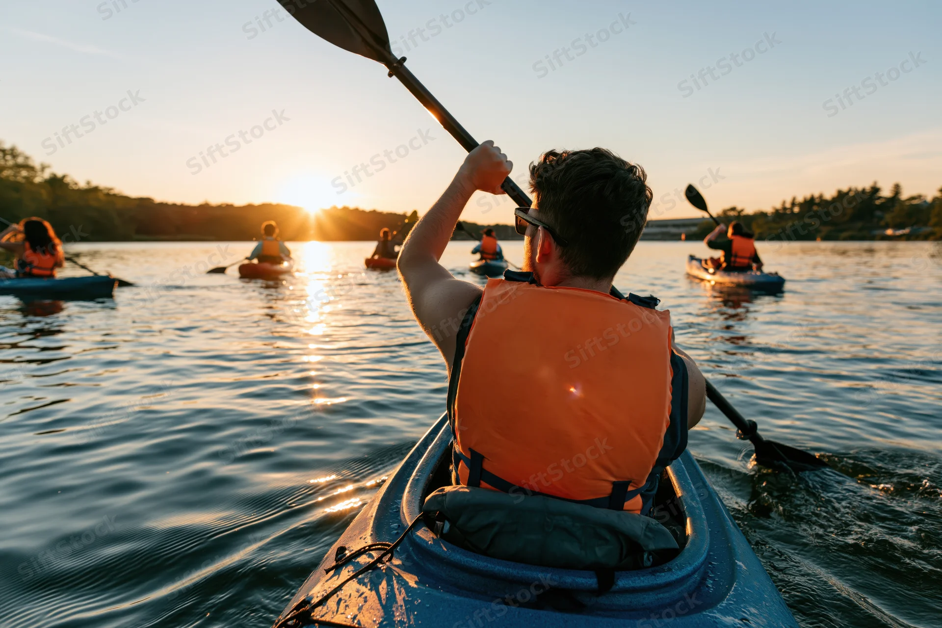 Man paddling kayak on calm river at sunset with group of kayakers ahead