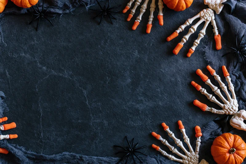 Halloween flat lay with skeleton hands, pumpkins and spiders arranged on dark slate stone surface with copyspace