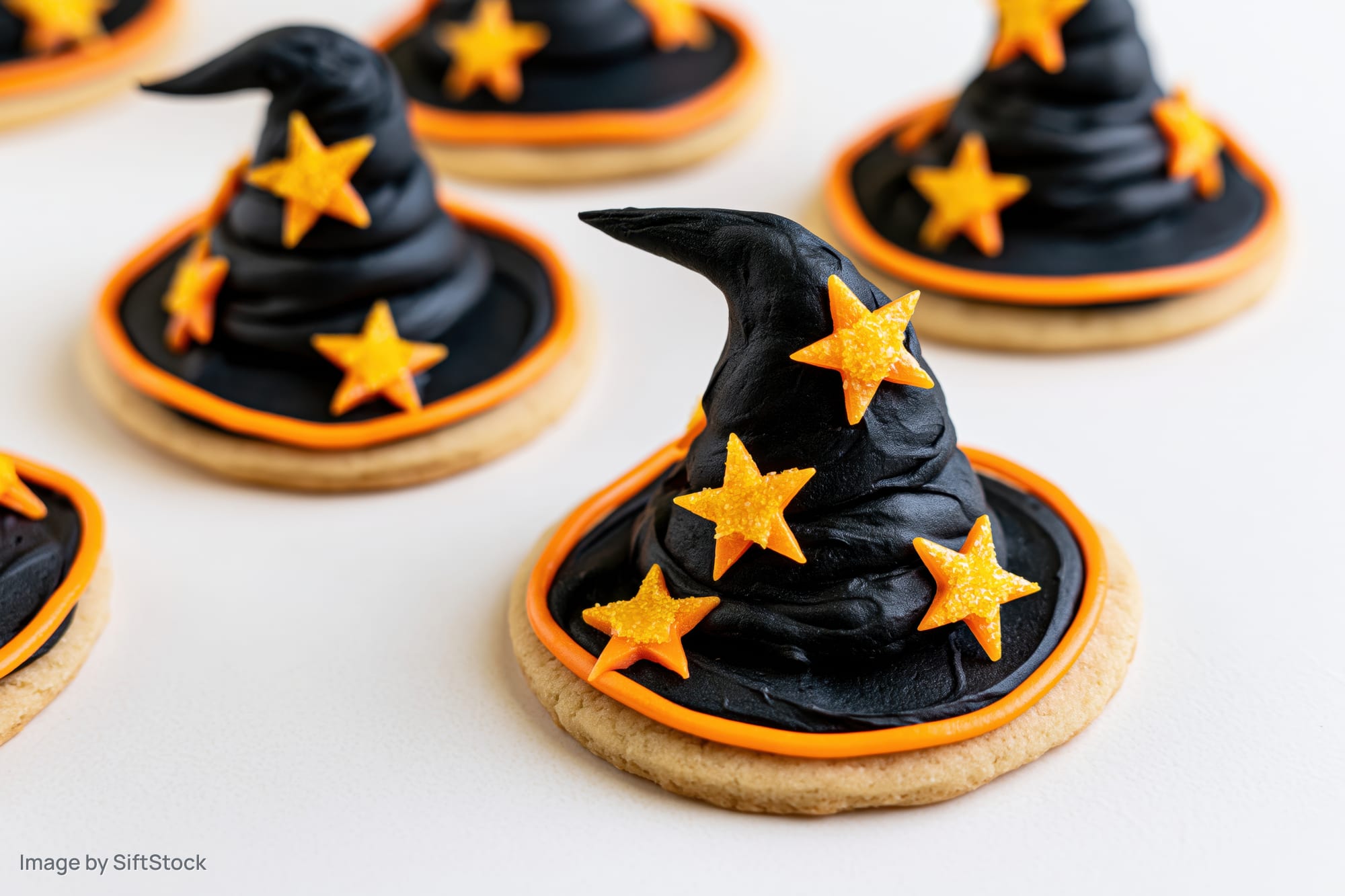 Witch hat sugar cookies decorated with black frosting and orange stars on white surface