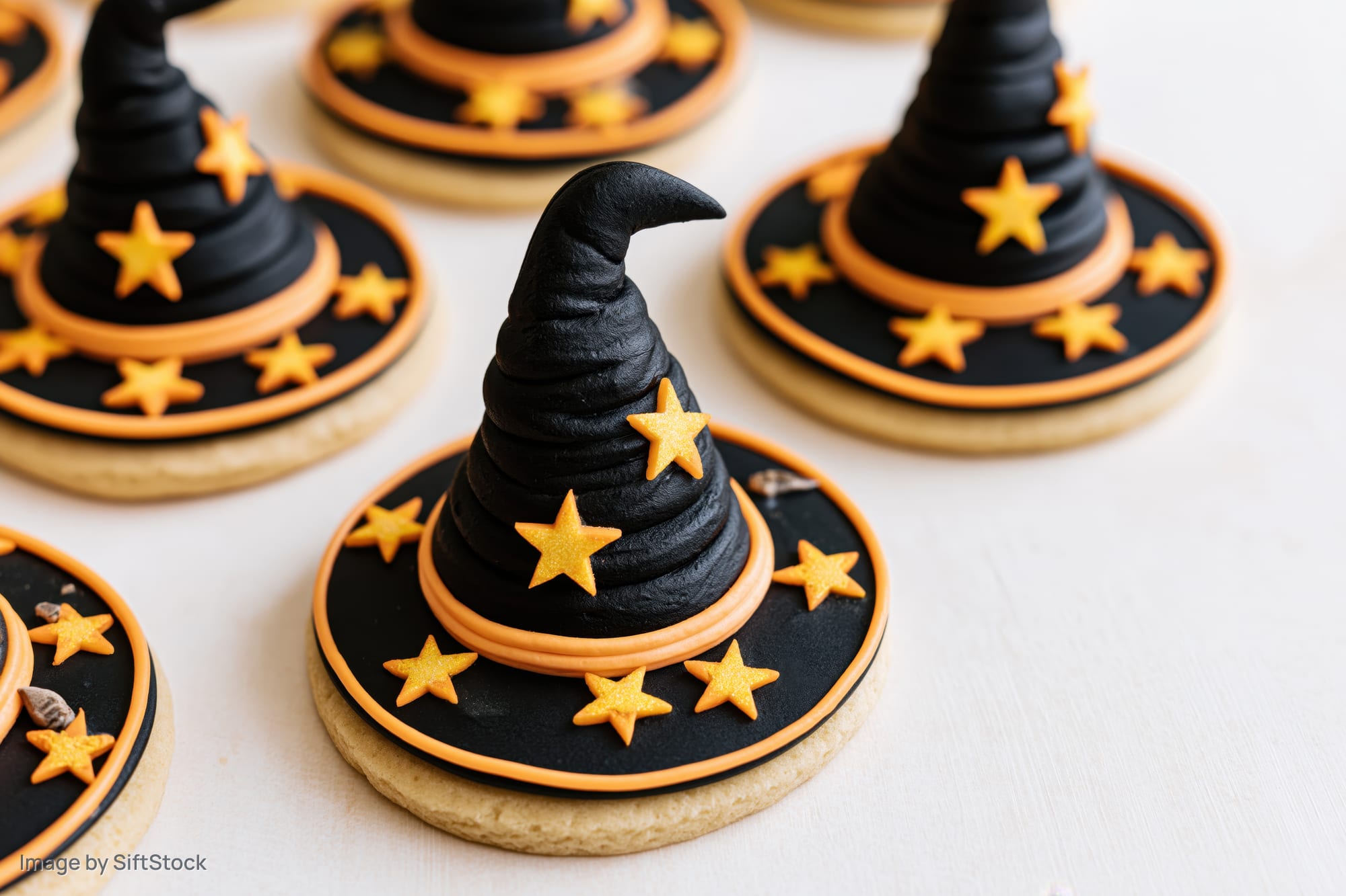 Witch hat sugar cookies decorated with black and orange frosting and stars arranged on a white surface