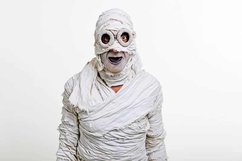 Man dressed as halloween mummy in white bandages facing camera with open mouth expression