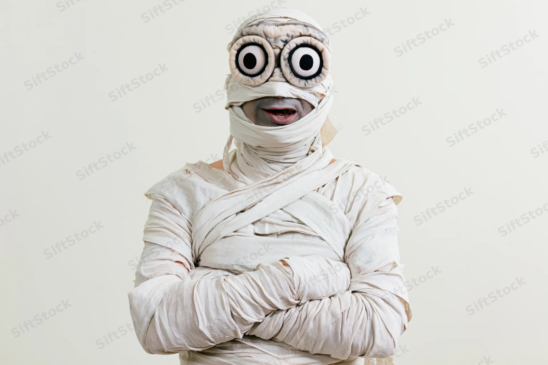 Man dressed as halloween mummy with arms crossed facing camera in studio