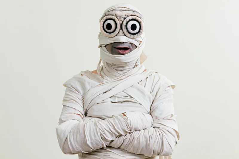 Man dressed as halloween mummy with arms crossed facing camera in studio