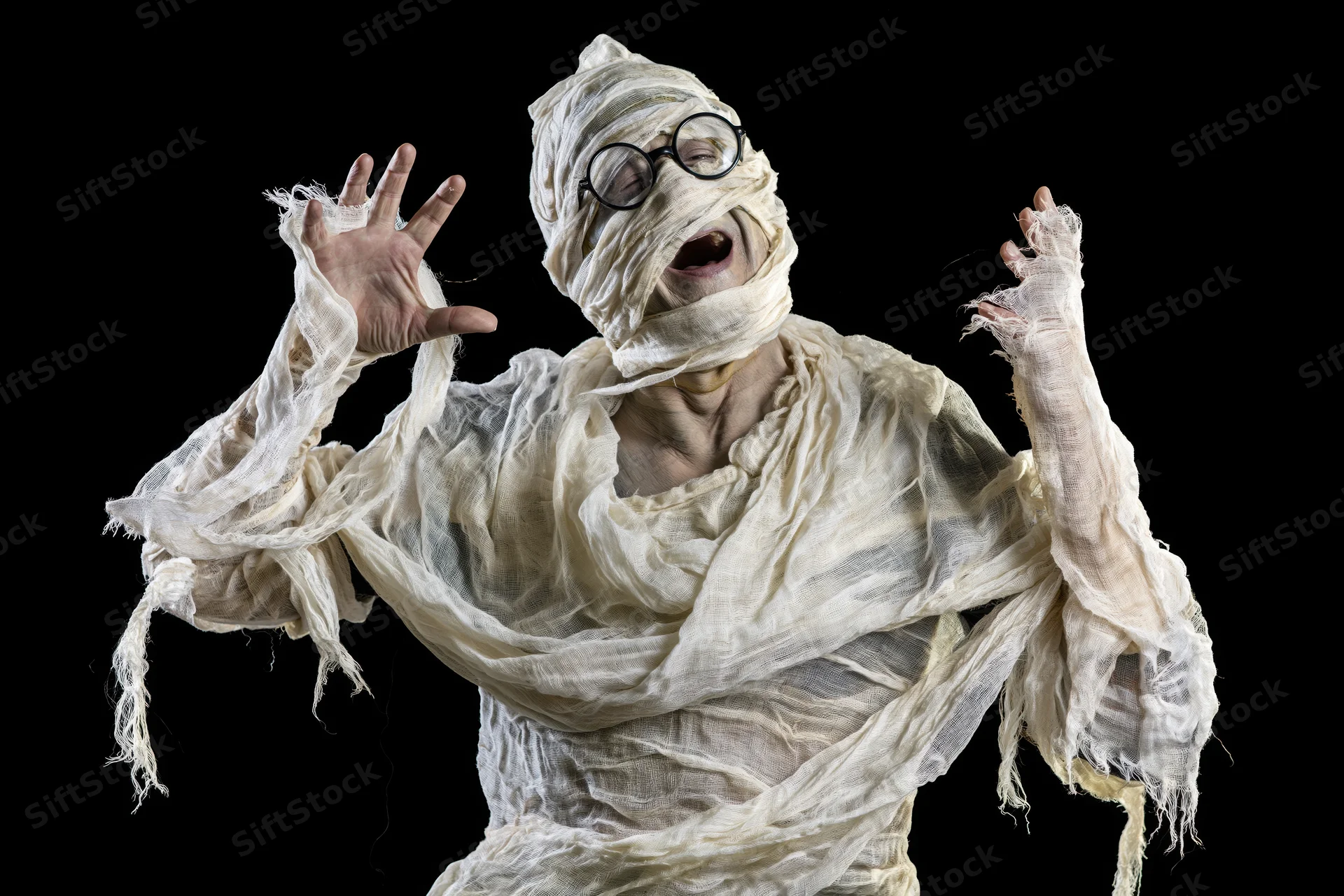 Man in homemade mummy costume laughing with arms raised against black background
