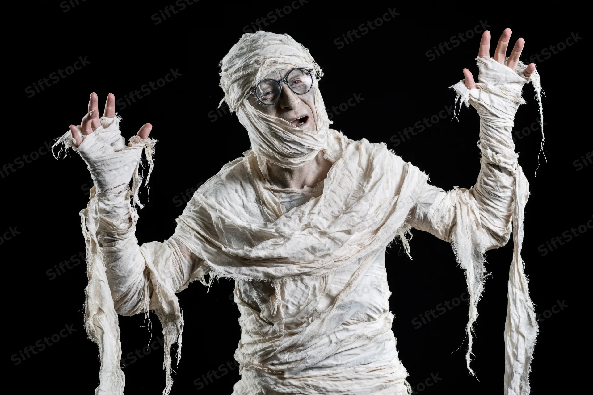 Man in homemade mummy costume laughing with arms raised against black background