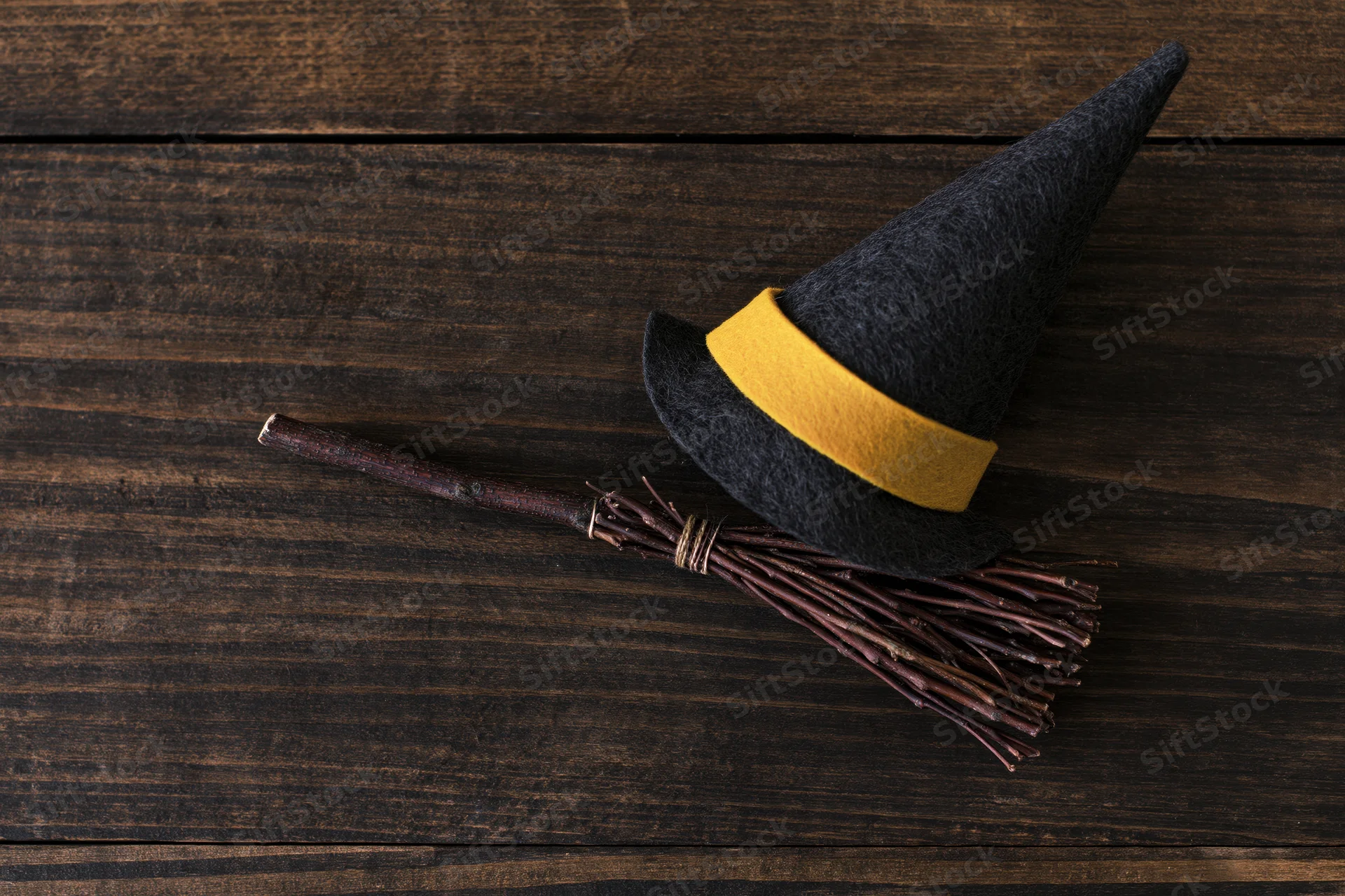 Witch hat with yellow band and small broom resting on dark wooden surface