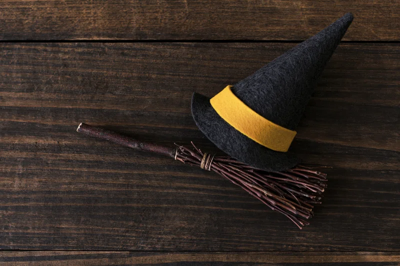 Witch hat with yellow band and small broom resting on dark wooden surface