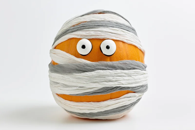 Orange pumpkin wrapped as a mummy with googly eyes on white background