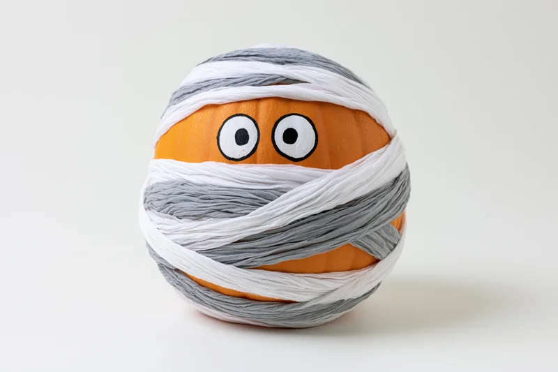 Orange pumpkin wrapped in white and gray bandages with painted eyes for halloween decoration