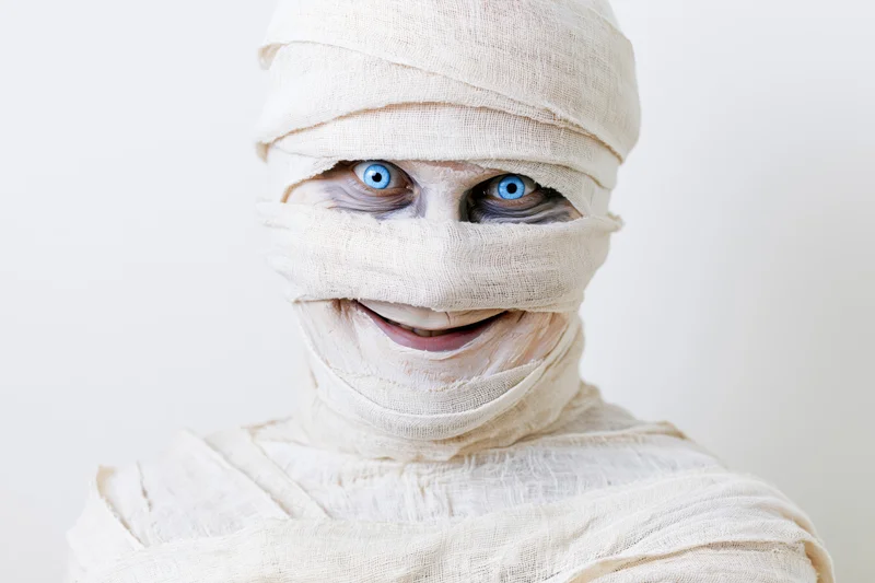Mummy in white bandages smiling with blue eyes against white background