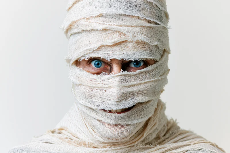 Person wrapped in white bandages with blue eyes visible, studio portrait