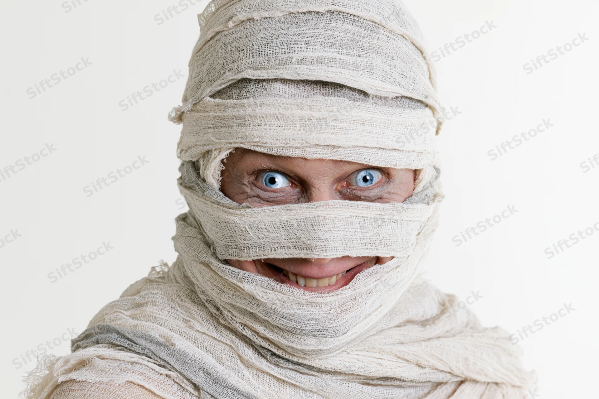 Woman dressed as a mummy with bandages wrapped around her head and face, smiling, isolated on white background