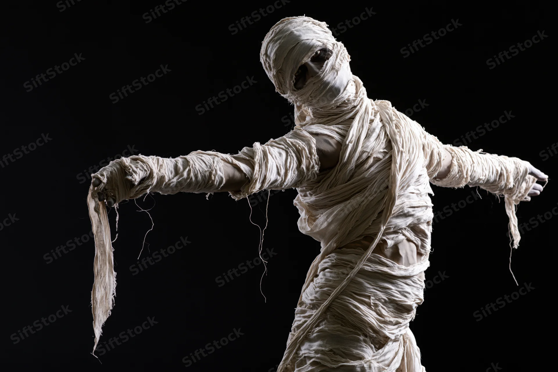 Person dressed as mummy with arms outstretched against black background