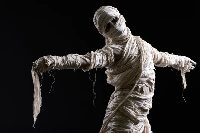 Person dressed as mummy with arms outstretched against black background