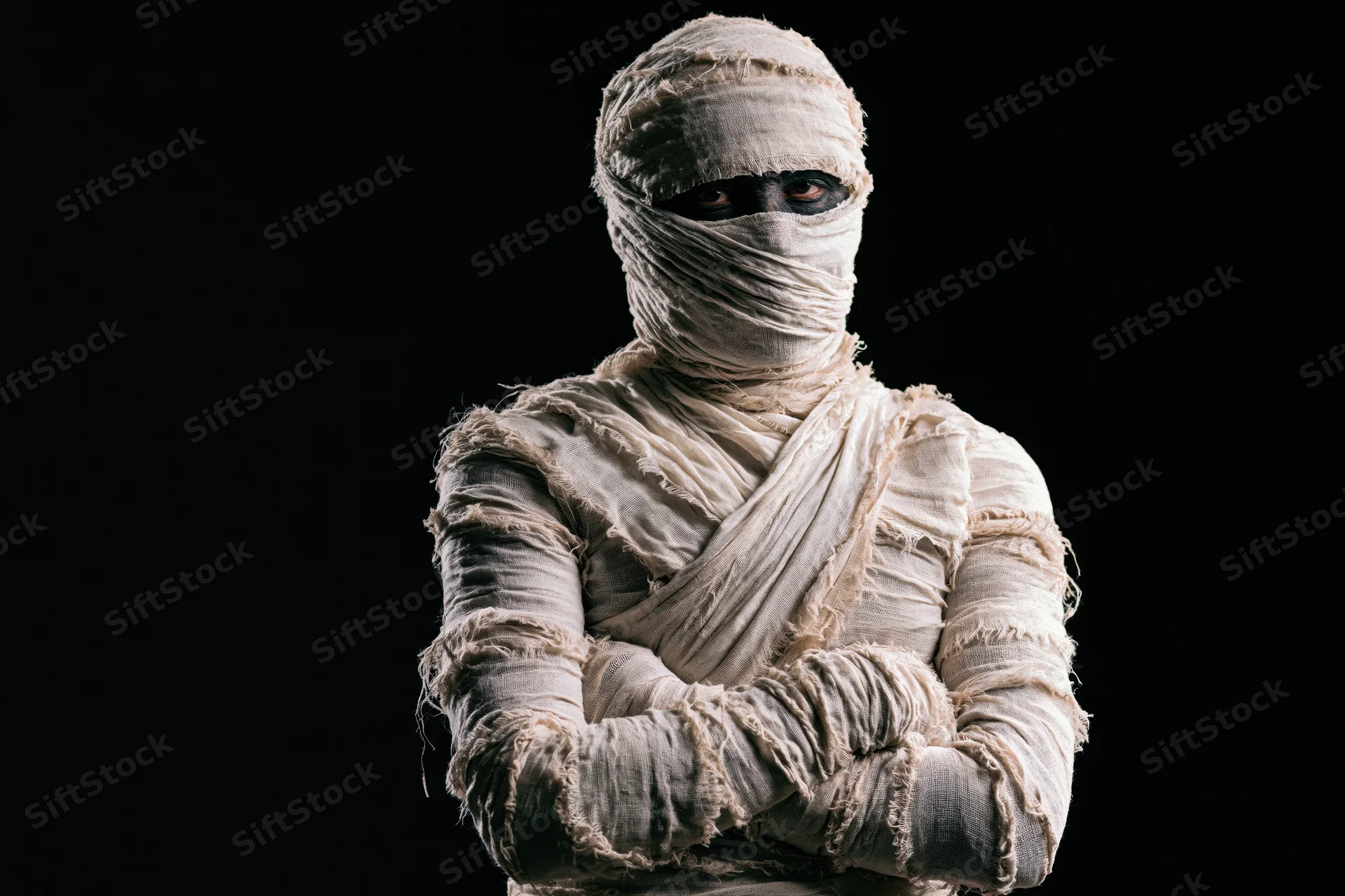 Man dressed as a mummy with arms crossed against black background