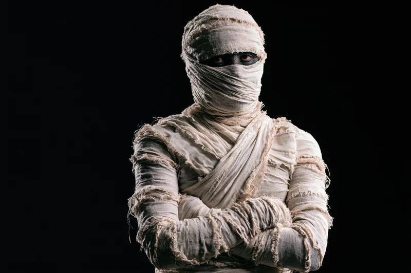 Man dressed as a mummy with arms crossed against black background