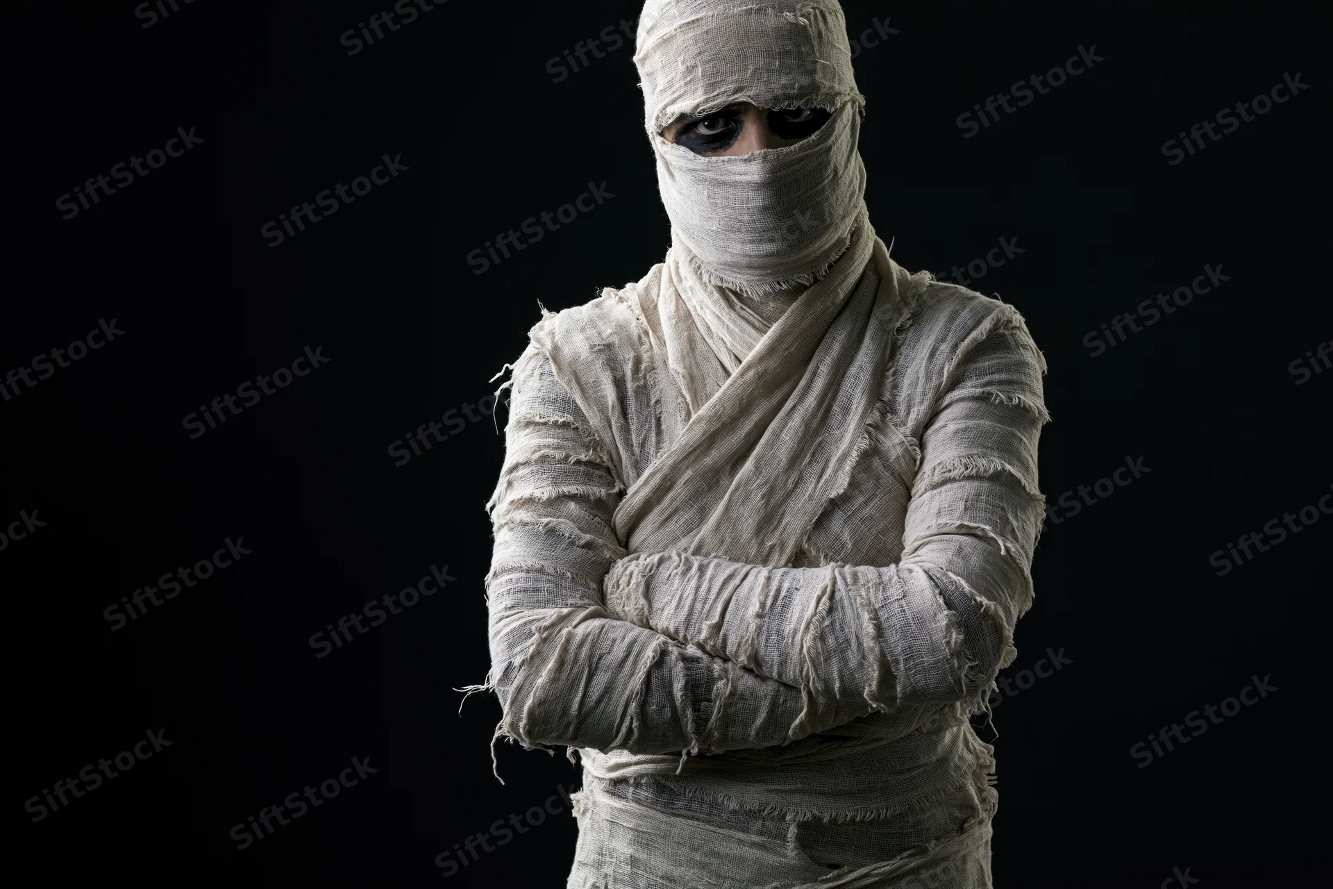 Mummy in white bandages standing with arms crossed against black background