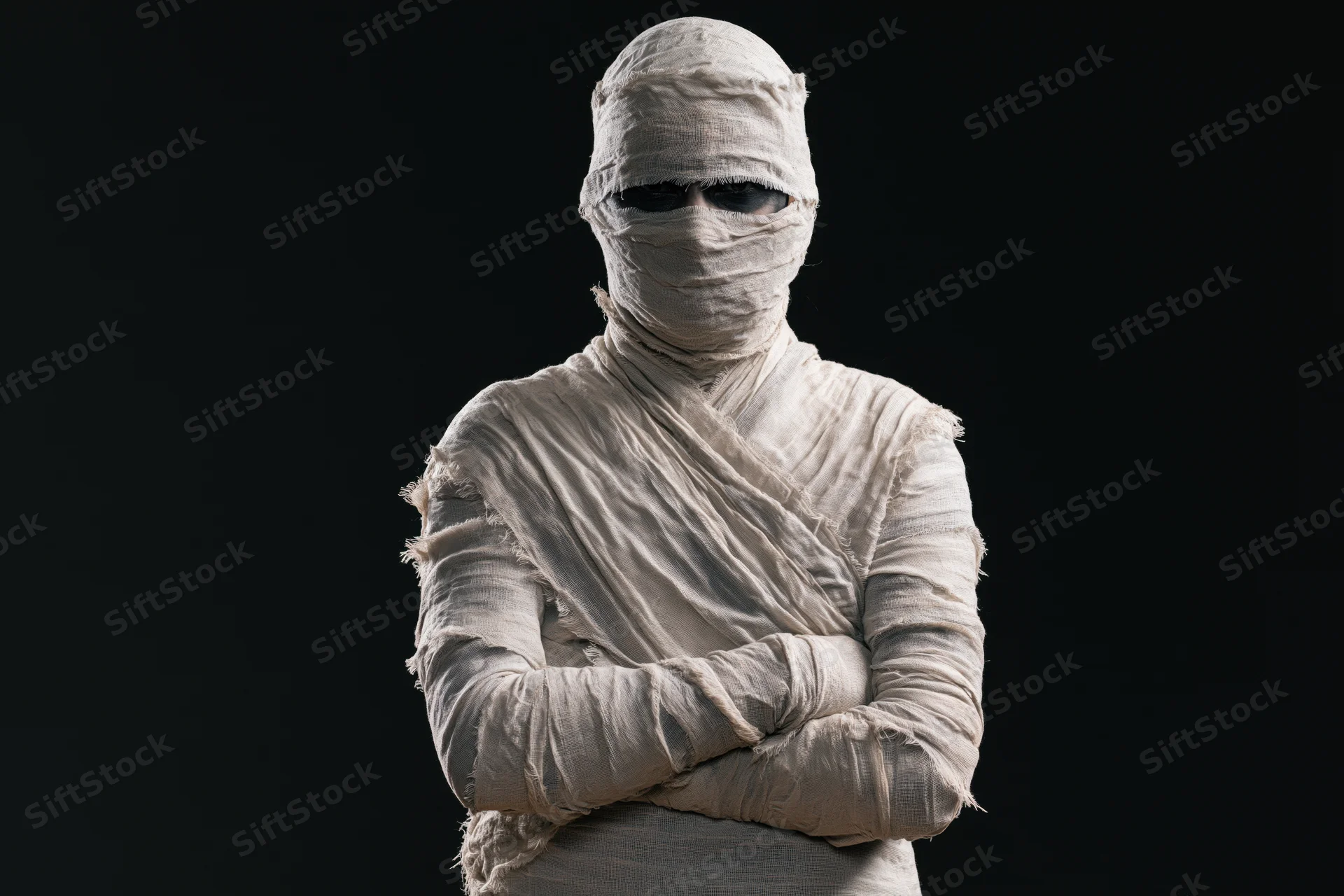 Mummy in white bandages with arms crossed against black background