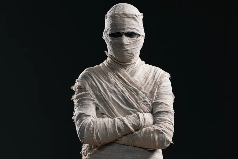 Mummy in white bandages with arms crossed against black background