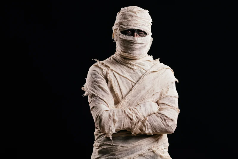 Mummy in white bandages standing with arms crossed against black background