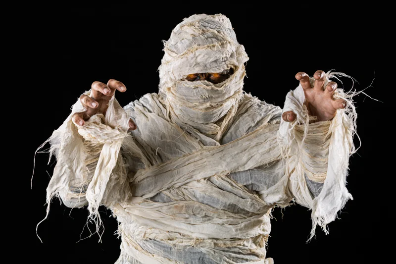 Mummy in white bandages reaching forward against black background