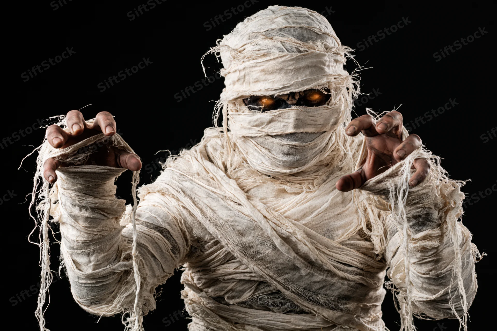 Mummy in tattered bandages with glowing eyes reaching forward against black background